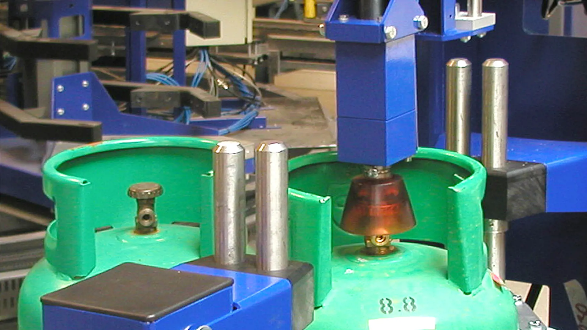 closeup of a valve opener and closer on a blue machine handling a green lpg cylinder