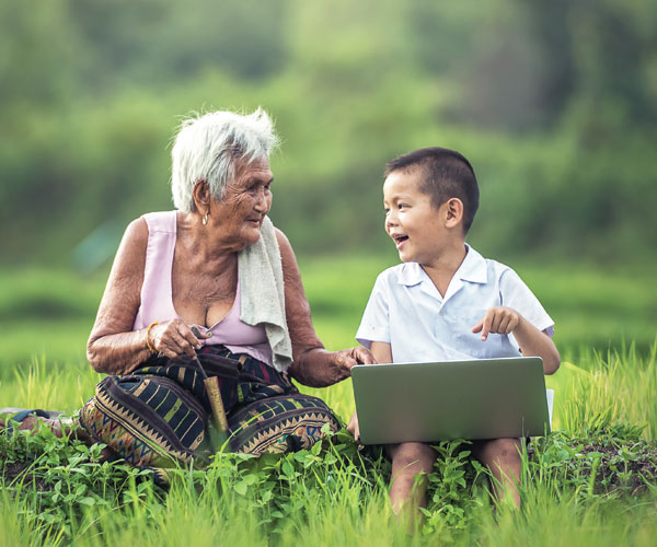 An elderly person and a child sitting together in a field with a computer