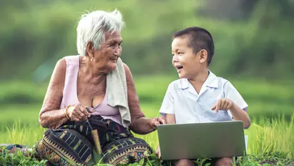 An elderly person and a child sitting together in a field with a computer