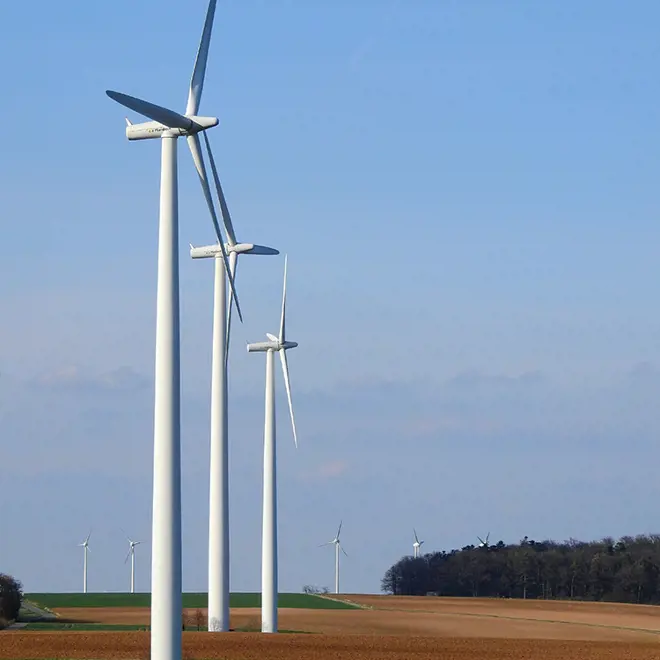 image of a brown and green field with white 3 wind turbines in front and 5 in the background blue sky
