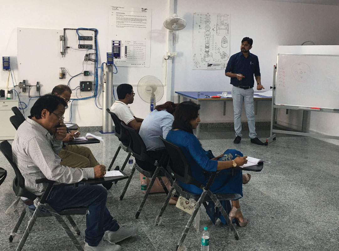 Image of people sitting on chairs while a man speaks to them standing infront of a whiteboard