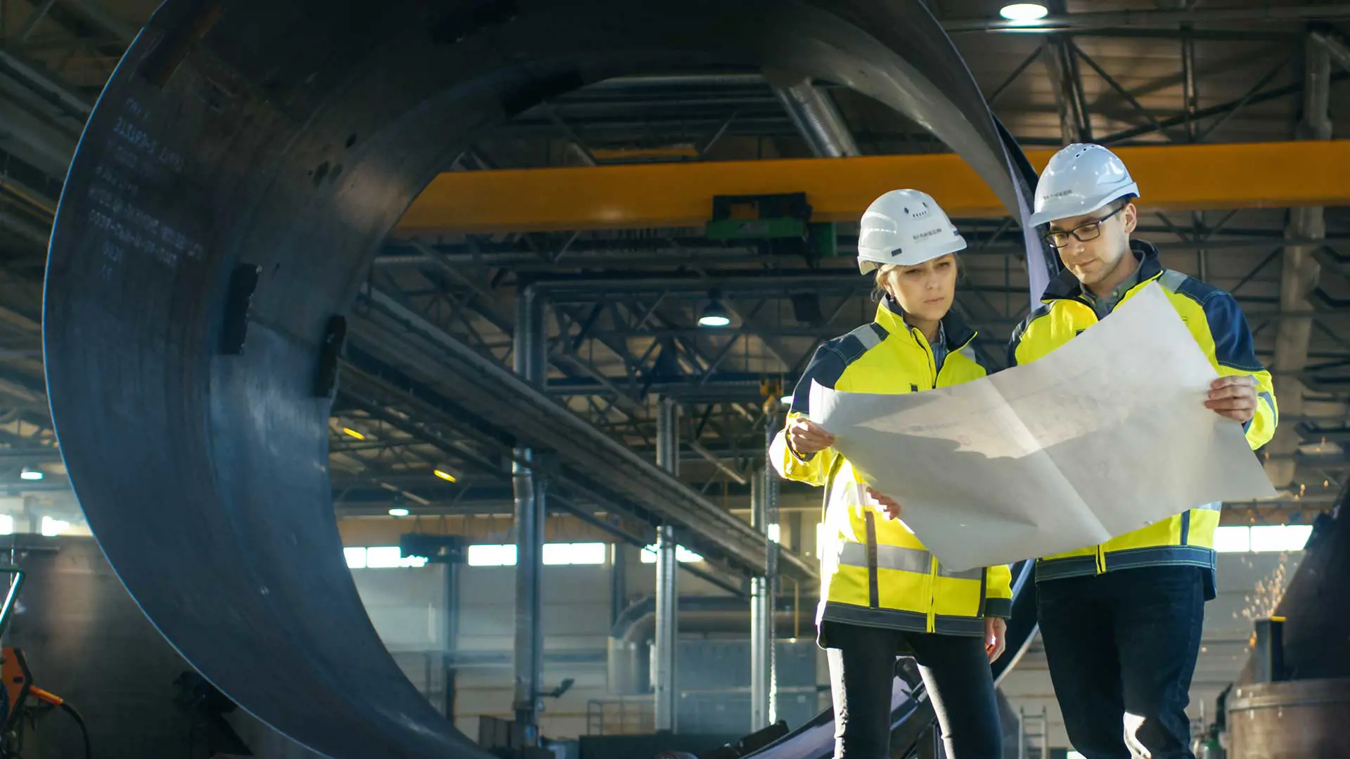 Man and woman in PPE looking at schematics in front of a steel tube