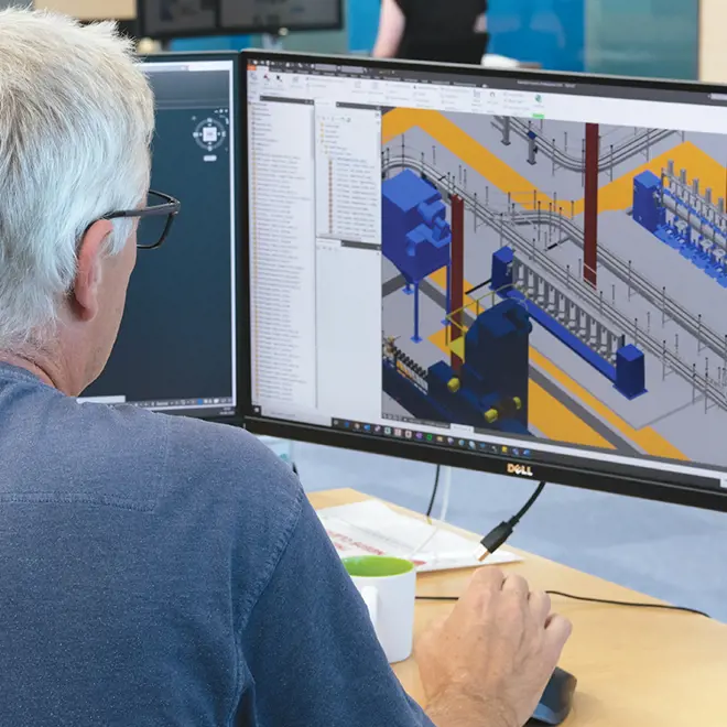 image of a greyhaired man from behind sitting at a desk infront of a screen drawing on a 3d illustration of a filling plant