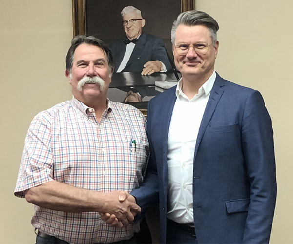 Skeeter LaDue shaking hands with Bo Larsen in front of a portrait of the first GEC CEO