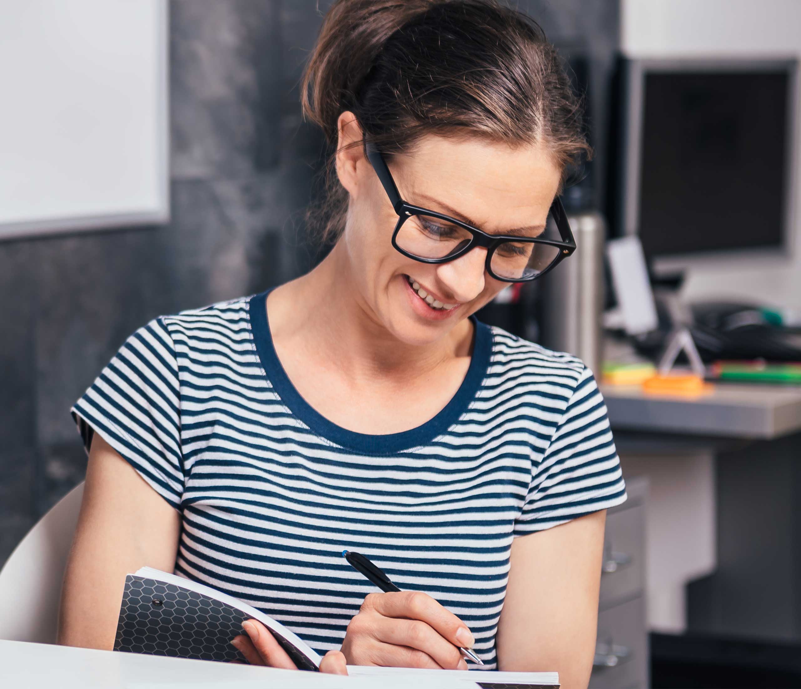 image of a smiling woman in stripes writing in a notebook