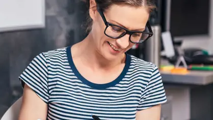 image of a smiling woman in stripes writing in a notebook
