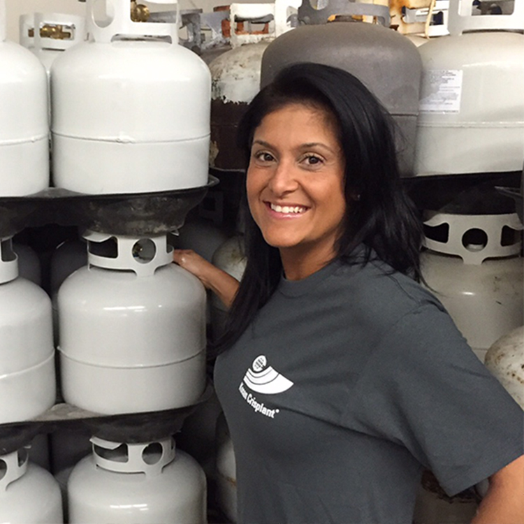 Portrait of a woman with t-shirt standing in front of several white LPG cylinders on shelfs CNB