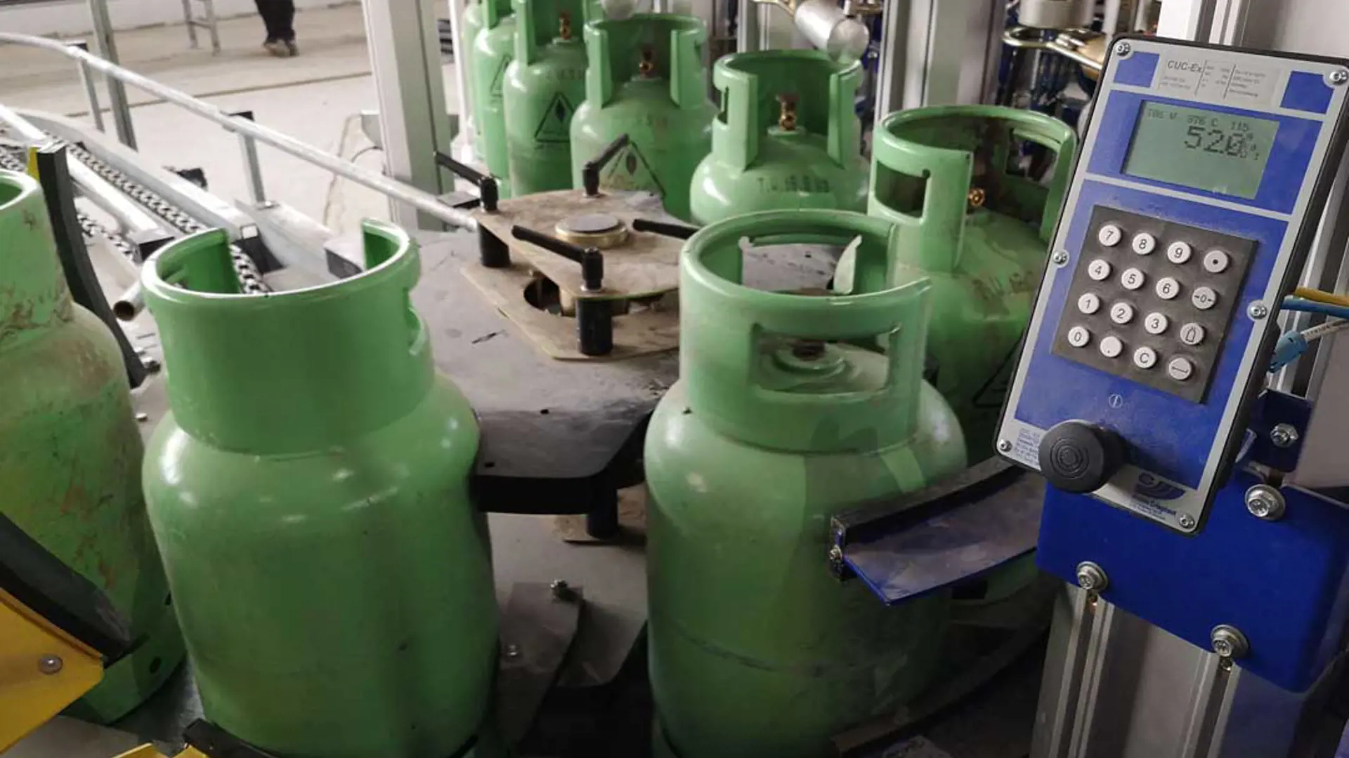 A picture showing gas cylinders on chain conveyer next to a modern controller.