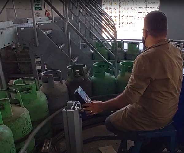 image of a worker using a crisplant universal controller and handling green lpg cylinders on a conveyor chain